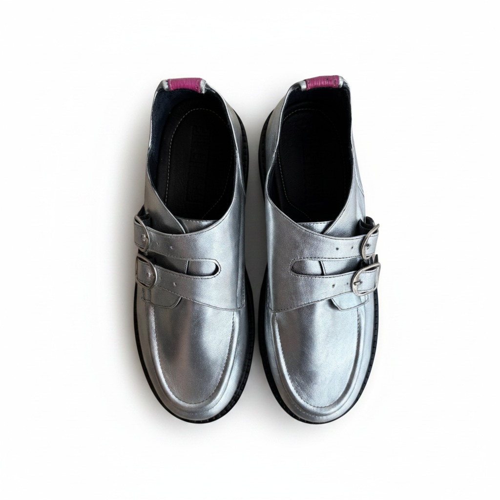 A pair of metallic silver leather double strap loafers with buckle details, shown from a top-down view on a white background.