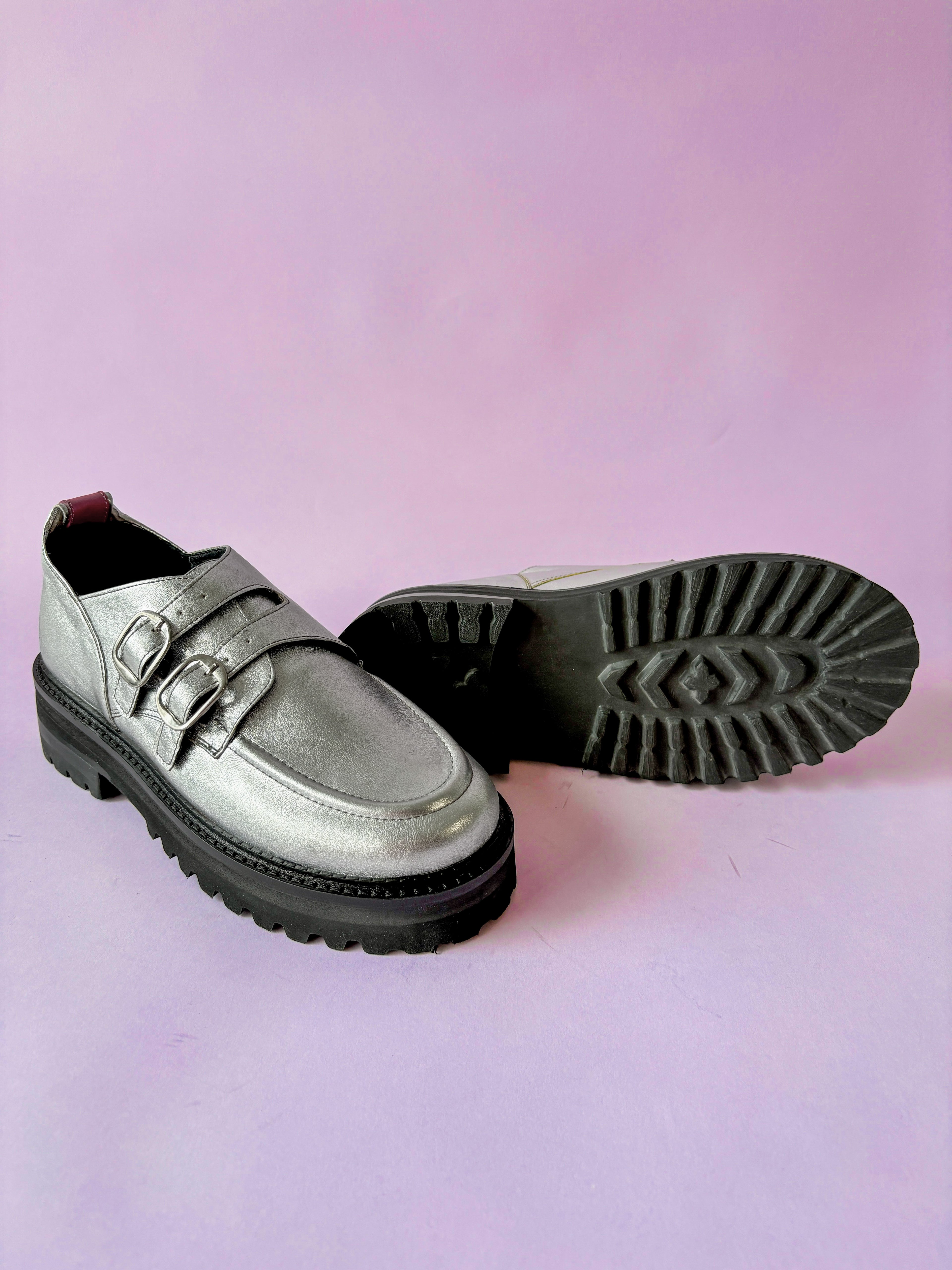 Silver loafers with black soles on a pink background