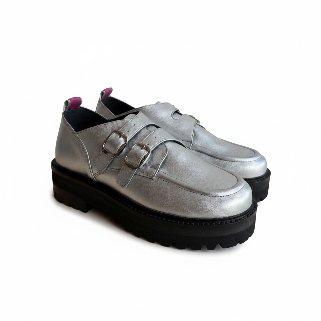 A pair of metallic silver leather double-strap loafers with chunky black lug soles, shown against a plain white background.